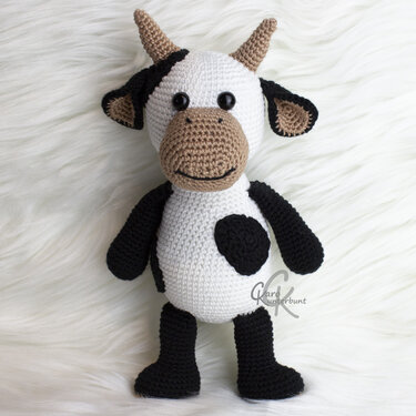 Gehäkelte Amigurumi-Kuh mit schwarz-weißem Fellmuster und beigen Hörnern.