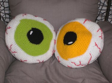 Zwei runde, gehäkelte Augenkissen mit grüner und gelber Iris und roten Adern