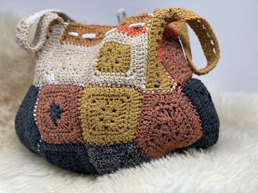 Granny-Square Shopper aus gehäkelten Quadraten in Senfgelb, Rost, Creme und Dunkelgrau auf flauschigem Untergrund