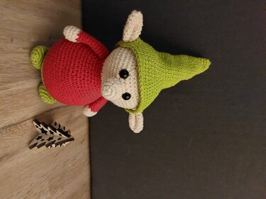 Gehäkelter Amigurumi-Wichtel in Rot und Grün neben kleiner Holz-Weihnachtsdeko