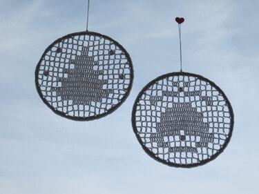 Zwei runde, gehäkelte Anhänger mit Weihnachtsbaum-Motiv vor hellem Himmel