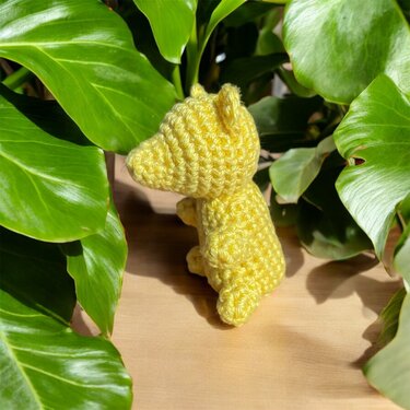 Gelbes gehäkeltes Amigurumi-Tier mit langer Schnauze vor grünen Blättern auf Holz