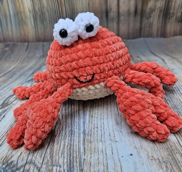 Gehäkelter korallenroter Krebs-Amigurumi mit weißen Kulleraugen und beigem Bauch
