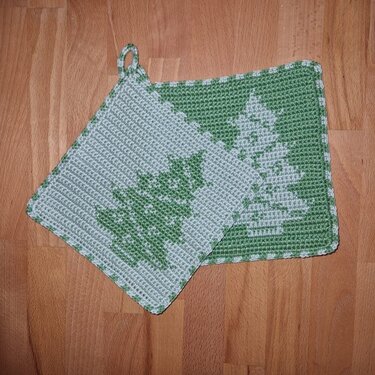 Zwei grüne gehäkelte Topflappen mit Tannenbaum-Motiv auf Holzuntergrund