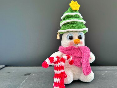 Niedlicher gehäkelter Schneemann mit Tannenhut, gelbem Stern, pinkem Schal und rot-weißer Zuckerstange