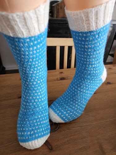 Zwei blaue gestrickte Socken mit weißen Punkten, weißen Bündchen und weißen Zehen auf einem Holztisch.