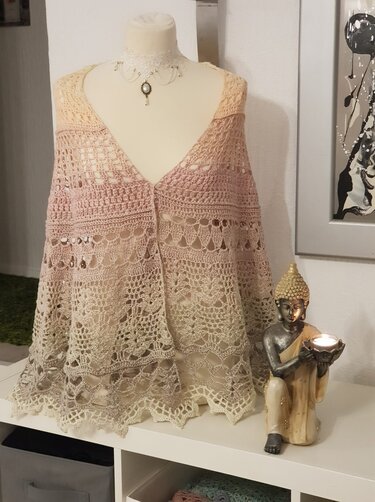 Gehäkeltes Halbrundtuch in Rosé und Creme mit Spitzenmuster auf einer Schneiderpuppe; daneben eine Buddha-Figur mit Teelicht.
