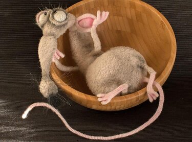 Nahaufnahme einer gehäkelten grauen Amigurumi-Maus mit rosa Schwanz in einer Holzschale