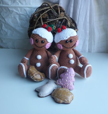 Zwei gehäkelte Lebkuchen-Amigurumi mit weißen Ziernähten und Plätzchen im Vordergrund