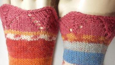 Zwei gestrickte Armstulpen mit bunten Streifen und zartem Ajourabschluss am oberen Rand.