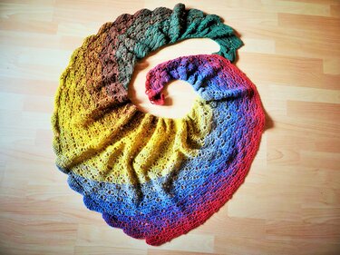 Gehäkeltes Spiraltuch mit Farbverlauf von Grün bis Rot und feinem durchbrochenem Lochmuster auf hellem Holzboden.