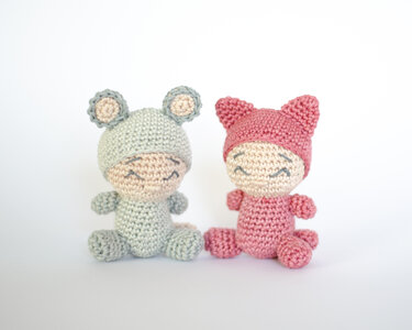 Zwei gehäkelte Amigurumi nebeneinander, links hellgrün mit runden Ohren, rechts rosa mit spitzen Katzenohren, beide mit gesticktem Gesicht
