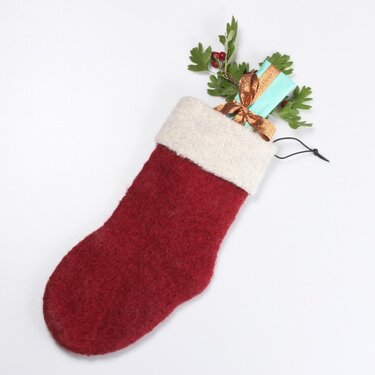 Red hand-felted Christmas stocking with white cuff holding a teal gift and greenery