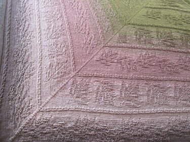 Nahaufnahme eines gestrickten Dreieckstuchs mit Blattmustern und Farbverlauf von Rosé zu Grün