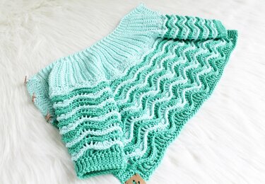 Mint green crocheted baby jacket laid flat showing ribbed yoke and ripple stitch body
