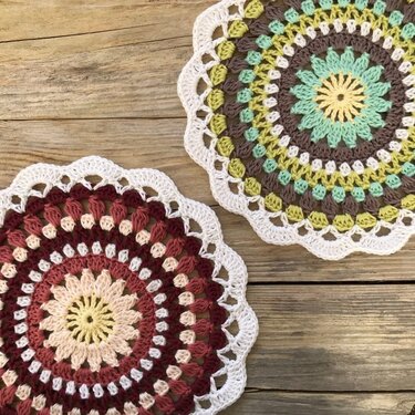 Two round crochet doilies with scalloped white edges and concentric textured stitches on wooden boards