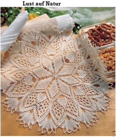 Rundes naturweißes Spitzendeckchen mit floralem Lochmuster auf Holztisch neben Serviette und Snacks.