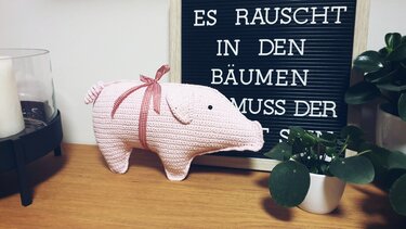 Rosa gehäkeltes Schwein mit rot-weiß karierter Schleife auf Holzoberfläche