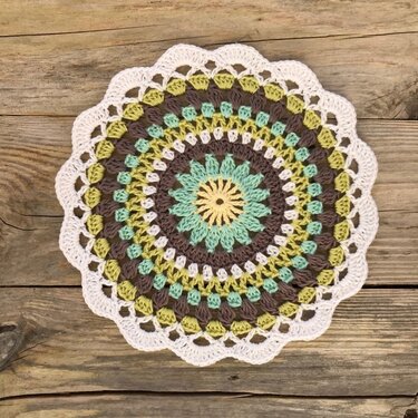 Round multicolored crocheted doily with scalloped edge on wooden planks