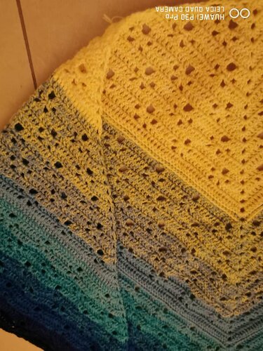 Gehäkeltes Dreieckstuch mit Farbverlauf von Gelb zu Blau und filigranem Lochmuster.