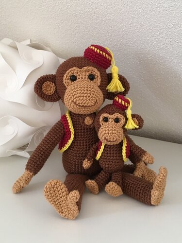 Zwei gehäkelte Amigurumi-Affen, groß und klein, mit braunen Körpern, beigen Gesichtern und rot-gelber Kleidung auf hellem Untergrund.