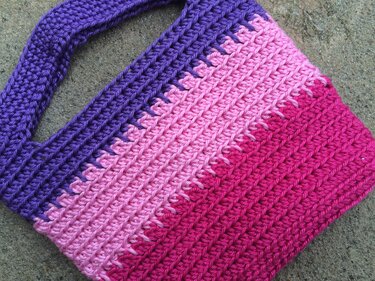 Gehäkelte Tasche mit Farbverlauf in Violett, Rosa und Pink auf Steinboden