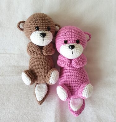 Zwei schlanke gehäkelte Amigurumi-Tiere in Braun und Rosa mit weißen Pfoten und kurzem Schwanz
