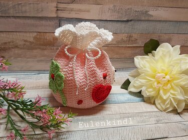 Gehäkeltes rosa Säckchen mit weißer Rüsche, rotem Herz, grünem Kleeblatt und Marienkäfern