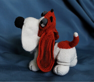Gehäkelter Basset Hound Amigurumi mit langen roten Schlappohren auf blauem Hintergrund