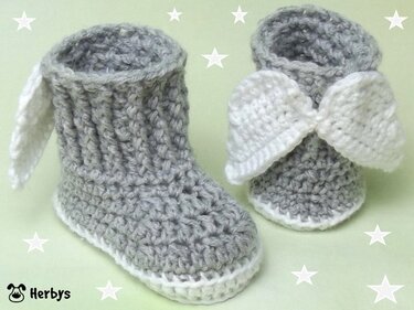Gehäkelte graue Baby-Stiefelchen mit weißen Engelsflügeln auf pastellgrünem Sternenhintergrund