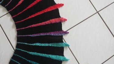 Schwarzer gestrickter Schal mit diagonalen, bunten Keilspitzen auf hellem Fliesenboden