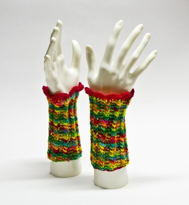 Fingerlose mehrfarbige gestrickte Armstulpen mit rotem Zackenrand an weißen Mannequinhänden