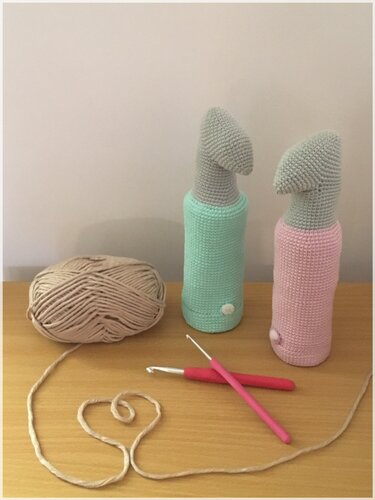 Zwei zylindrische gehäkelte Utensilos in Mint und Rosa mit Garnknäuel und Häkelnadeln auf einer Tischfläche