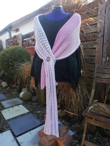 Gehäkelte Stola in Rosa und Weiß mit offenem Gittermuster, an einer Schneiderpuppe mit Brosche drapiert.