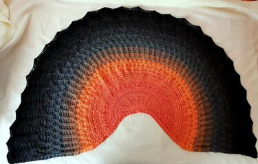 Handgearbeitetes halbrundes Tuch mit Farbverlauf von Schwarz über Grau zu Orange und Rot‑Orange, mit wellenförmiger Kante.