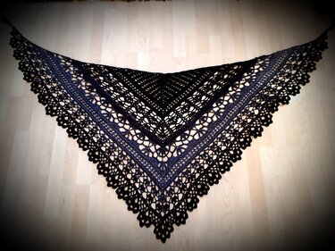 Gehäkeltes Dreieckstuch in Schwarz und Dunkelblau mit Spitzenmuster auf hellem Holzboden.