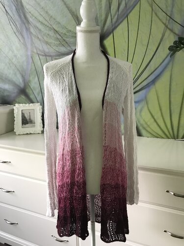Mannequin trägt lange offene Strickjacke mit Ombre-Verlauf von Weiß über Rosa bis Burgunder und Lochmuster am Saum