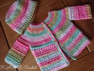Pastel striped crocheted baby cardigan and matching hat laid flat on wooden surface