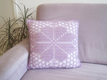 Quadratischer lilafarbener Kissenbezug mit gehäkeltem Herzmuster auf einem Sofa