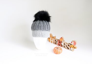 Two-tone grey crochet hat with a black pompom on a white mannequin head against a white background.