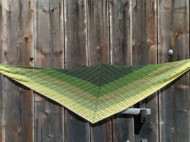 Gestricktes Dreieckstuch mit grünem Farbverlauf und Ajourlöchern an einer Holzwand