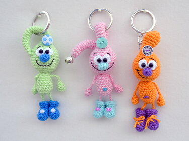 Drei gehäkelte AmigurumiSchlüsselanhänger in Grün, Rosa und Orange mit Stiefeln und Metallringen