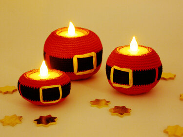 Three red crocheted Santa belt candle holders with glowing LED lights and scattered wooden star cutouts on a light surface.