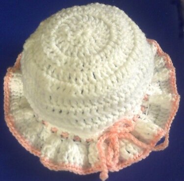 Weiße gehäkelte Babymütze mit rosa Rüschenrand und Bindekordel