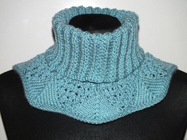 Türkis gestrickter Kragenschal mit hohem Rippenkragen und Lochmuster auf dunkler Büste.