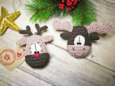 Zwei gehäkelte Elche in Braun und Rosa als Weihnachtsanhänger auf hellem Holzhintergrund mit Tannenzweigen