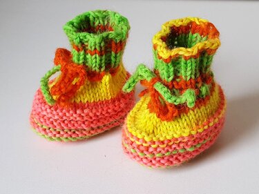 Bunte gestrickte Babyschuhe in Grün, Gelb, Orange und Rosa auf hellem Hintergrund