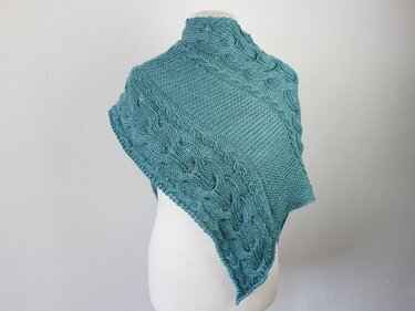 Teal knitted triangle shawl with braided cable border draped on a white dress form
