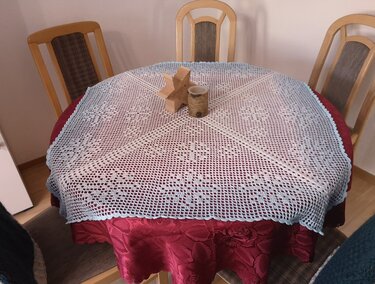 Rundes hellblaues gehäkeltes Deckchen mit Blumenmuster auf rotem Tisch