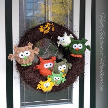 Dunkler Naturkranz mit sieben gehäkelten Amigurumi-Eulen in verschiedenen Farben, an einer Haustür hängend